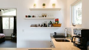 Uma cozinha moderna com armários brancos, uma máquina de café e uma janela com vista para o verde.