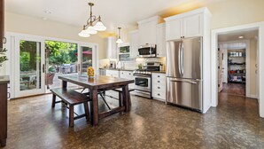 A spacious kitchen with white cabinets, stainless steel appliances, and a wooden dining table. - The St. Helena House (Saint Helena)