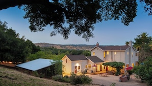 A two-story house with a covered patio, a small detached garage, and a view of the surrounding hills. - The St. Helena House (Saint Helena)