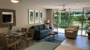 Een moderne woonkamer met een bank, fauteuils, een eettafel en een groot raam met uitzicht op groen.