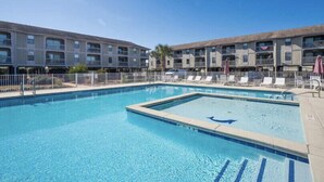 Ein rechteckiger Pool mit Hai-Motiv, umgeben von einem Zaun, neben einem mehrstöckigen Gebäude mit Balkonen.