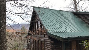 Eine Blockhütte mit einem grünen Metalldach, einer Holzdiele und Blick auf Berge im Hintergrund.