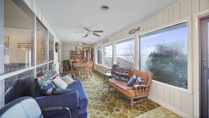A spacious room with a large window, a ceiling fan, and a dining area with wooden chairs and a table.