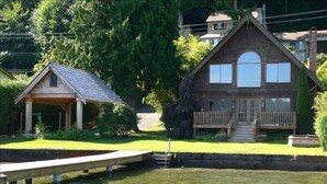 A house with a dock extending into a clear water body, surrounded by lush greenery. - Lake Whatcom Beach Resort (Bellingham)