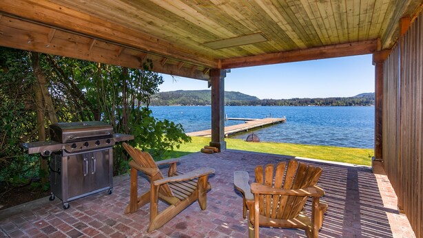 An outdoor patio with a grill, two Adirondack chairs, and a view of a lake. - Lake Whatcom Beach Resort (Bellingham)