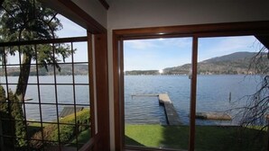 A room with a large window overlooking a lake, a dock, and a distant shoreline with hills. - Lake Whatcom Beach Resort (Bellingham)