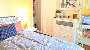 A bedroom with a bed, bedside table, lamp, dresser, and a door leading to a bathroom. - Steps to the water on both sides!! Mango Tango (San Diego)