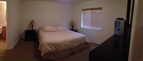 A bedroom with a bed, bedside lamps, a window with blinds, and a bathroom with a shower curtain.