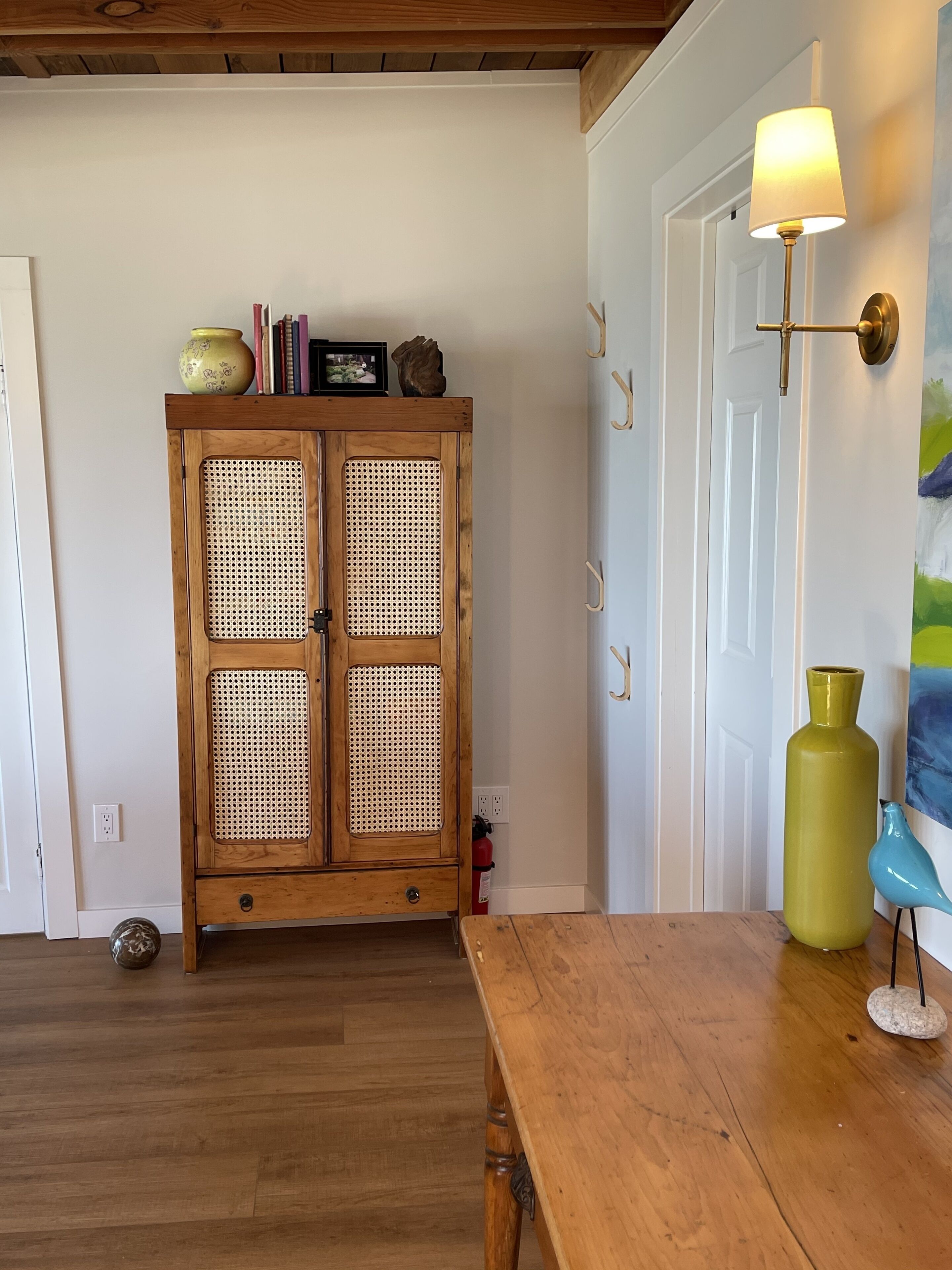 Un armario de madera con puerta de ratán, una mesa de madera, una lámpara y un jarrón en el suelo.