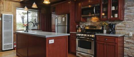 A kitchen with wooden cabinets, a central island, stainless steel appliances, and a stone accent wall.