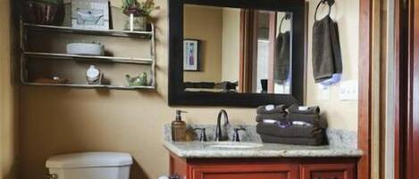 A bathroom with a toilet, a vanity with a mirror, and shelves above the toilet.