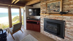 A living room with a fireplace, a television, and a view of the ocean.