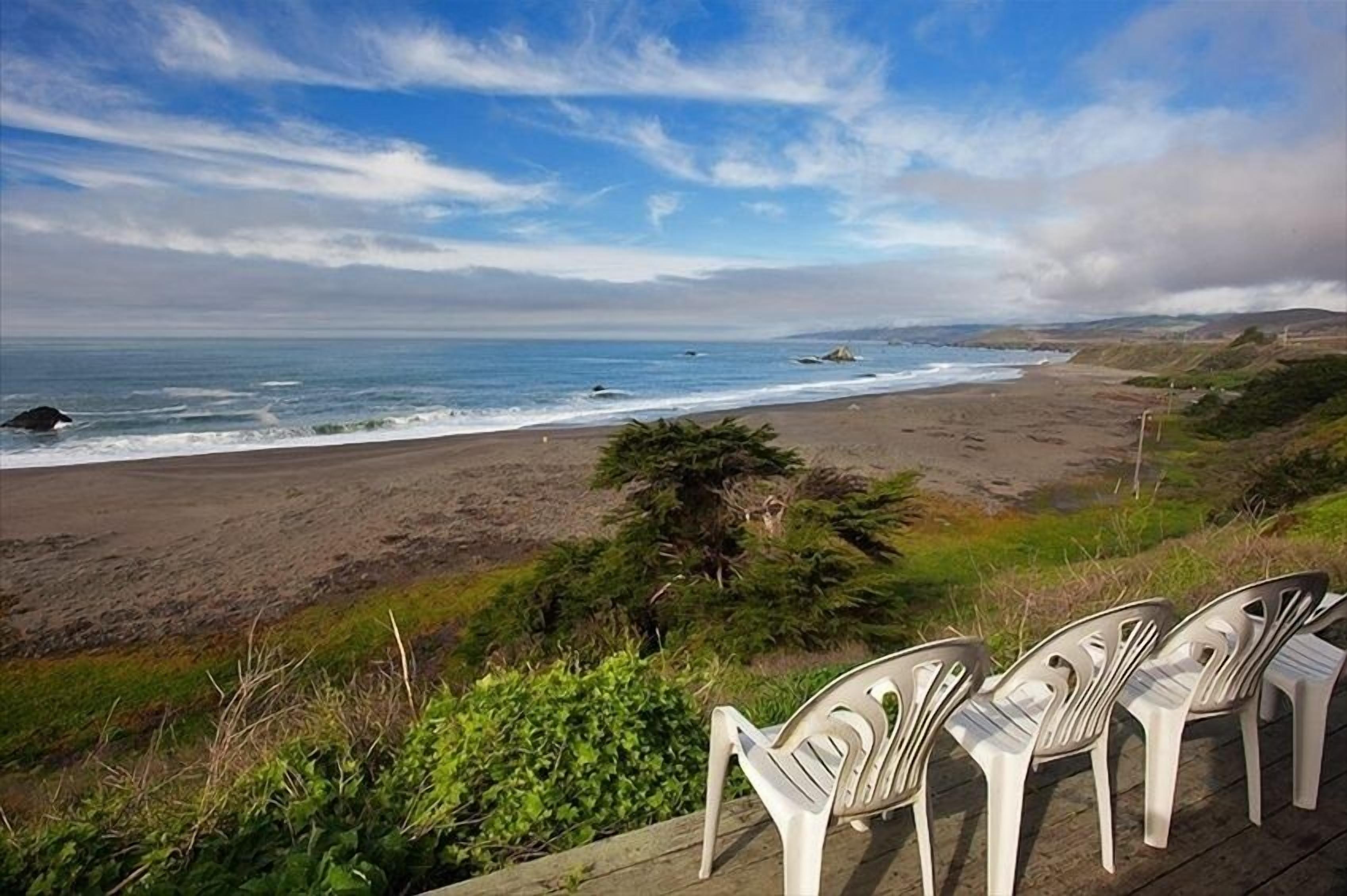 Una playa con una terraza de madera y sillas de plástico frente al océano.