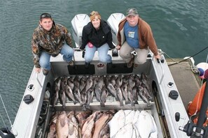 Three people on a boat with a large catch of fish.