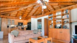 Ein gemütliches Wohnzimmer mit Holzbalkendecke, einer Couch, einem Couchtisch und integrierten Bücherregalen.