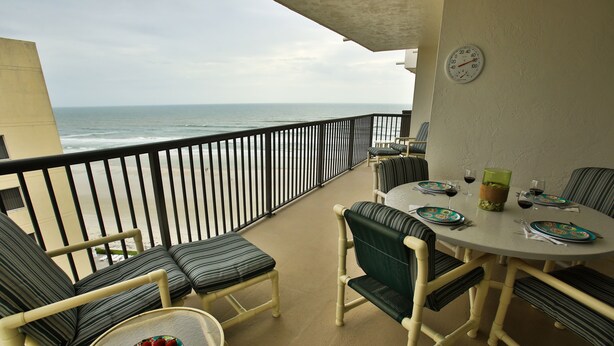 Varanda com vista para o oceano, decorada com cadeiras listradas e uma mesa posta para refeições.