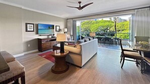 Una sala de estar moderna con sofá, mesa de centro y televisor. Cuenta con un balcón con vistas a zonas verdes y edificios.