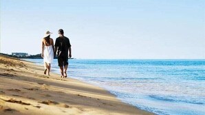 Una pareja caminando por una playa con cielo despejado.