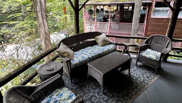 A covered outdoor seating area with wicker furniture, a patterned rug, and a hanging light fixture. - Cozy Mount Gretna Chautauqua Cottage near Hershey with treehouse porch  (Mount Gretna)