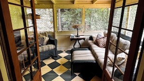 A cozy room with a checkered floor, a sofa, a chair, and a table with a lamp. - Cozy Mount Gretna Chautauqua Cottage near Hershey with treehouse porch  (Mount Gretna)