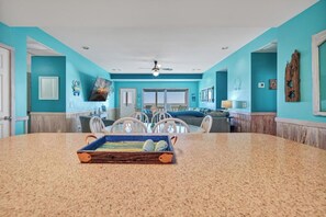 A spacious room with a large granite table, a ceiling fan, and a view to the outside.