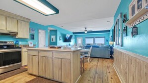 A kitchen with wooden cabinets, a central island, and a dining area with a blue couch. - 4BR/4Bth Direct Oceanfront,House,Covered Porch and fireplace! (Edisto Beach)