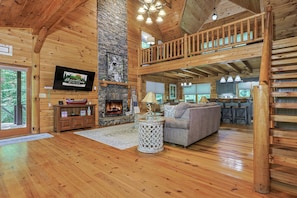 A wooden interior with a fireplace, a sofa, a dining area, and a TV mounted on the wall. - Rockin' River by Mountain Oasis | Trout Fishing Cabin Coosawattee (Ellijay)