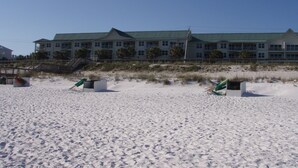 Ein Strandhotel mit Gründach, mehreren Balkonen und einem Sandstrand im Vordergrund.