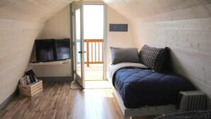 A cozy attic bedroom with a bed, a TV, and a wooden floor. - For less than two hotel rooms, stay on the Spit and sleep 7!  (Homer)