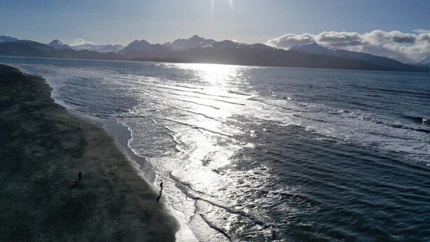 A beach with a clear view of mountains in the background and the sun reflecting off the water. - For less than two hotel rooms, stay on the Spit and sleep 7!  (Homer)