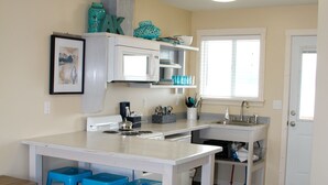 A compact kitchen with a white countertop, blue bar stools, a microwave, and a sink. - For less than two hotel rooms, stay on the Spit and sleep 7!  (Homer)
