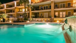 Un hotel de varios pisos con piscina, mobiliario exterior y palmeras.