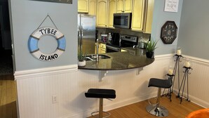 Una cocina con una isla curva, dos taburetes de bar, un letrero de salvavidas y un letrero de bienvenida.