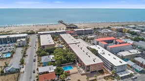 An aerial view of a coastal resort area with multiple buildings, a beach, and a pier.