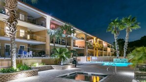Un hotel de varios pisos con piscina, palmeras y zonas de estar al aire libre.