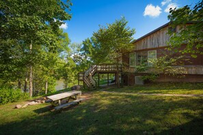 A rustic cabin with a wooden deck and picnic table, surrounded by lush greenery and a clear sky. - Captain's Lodge 15 Acres w/300 Meters Of Private Shenandoah Riverfront property (Luray)