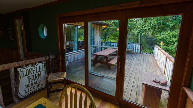 A wooden deck with picnic tables and chairs, a glass door leading outside, and a sign reading "Lorelai Farm Donald Liscomb".