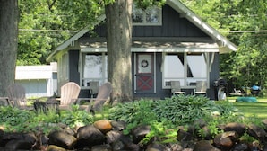 En hytte med veranda, to Adirondack-stole, et lille bord og en grill.