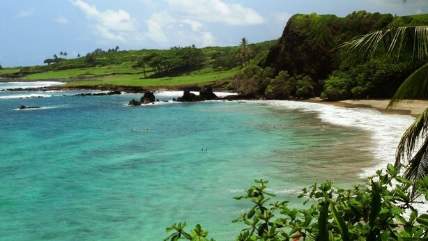 A coastal landscape with clear turquoise waters, a sandy beach, and lush greenery. - Beautiful Home in paradise! (Hana)