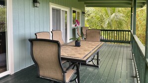 A covered porch with a table and four chairs, a potted plant, and a view of tropical foliage. - Beautiful Home in paradise! (Hana)