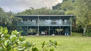 A two-story building with a balcony, surrounded by lush greenery and a grassy lawn. - Beautiful Home in paradise! (Hana)