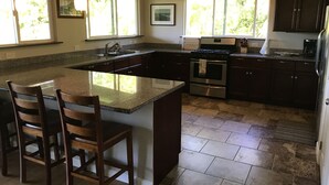 A spacious kitchen with a large island, dark wooden cabinets, and a stainless steel oven. - Beautiful Home in paradise! (Hana)