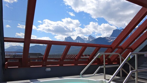 Ein Whirlpool mit Blick auf die Berge, rote Geländer und ein klarer Himmel.