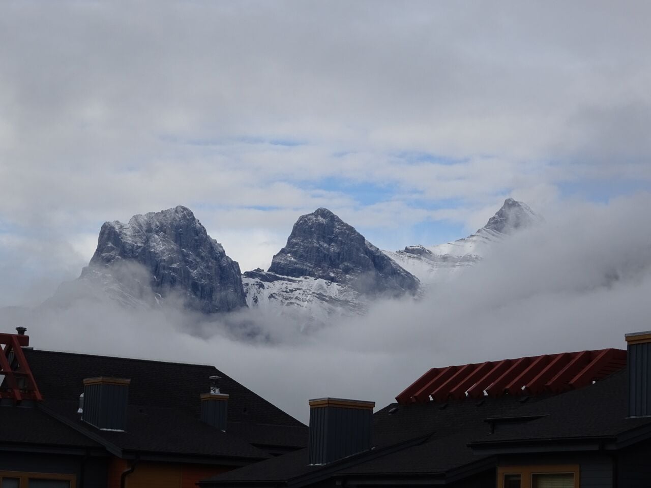 Catena montuosa con cime innevate parzialmente nascoste dalle nuvole, con edifici in primo piano.