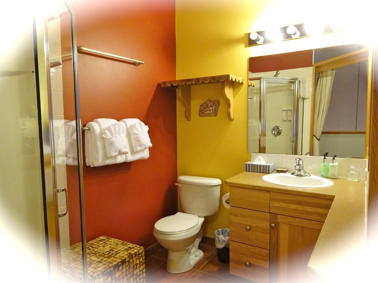 A bathroom with a glass shower enclosure, a toilet, a sink with a mirror, and a towel rack with white towels.