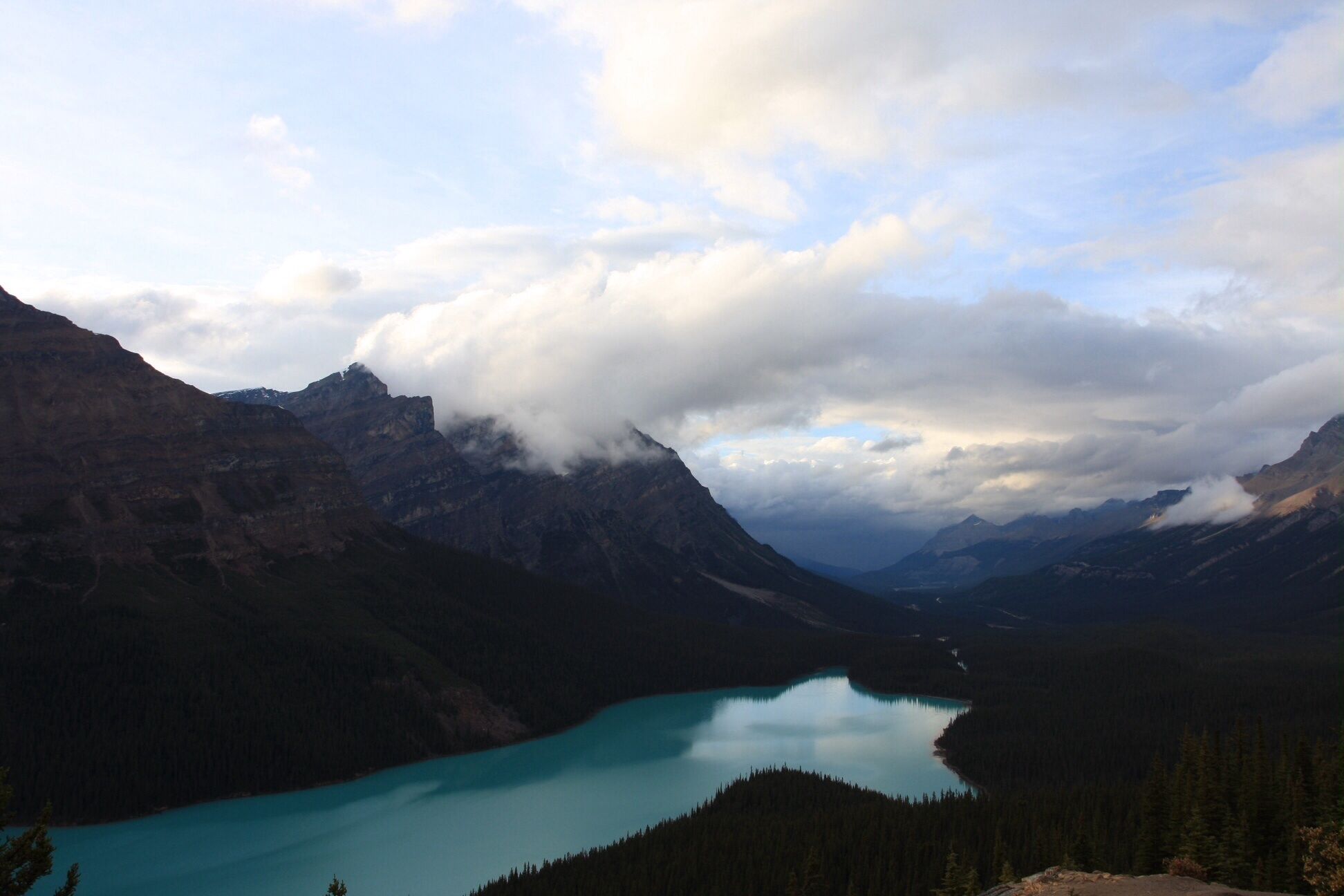 A mountain landscape with a turquoise lake surrounded by dense forests and rugged peaks.