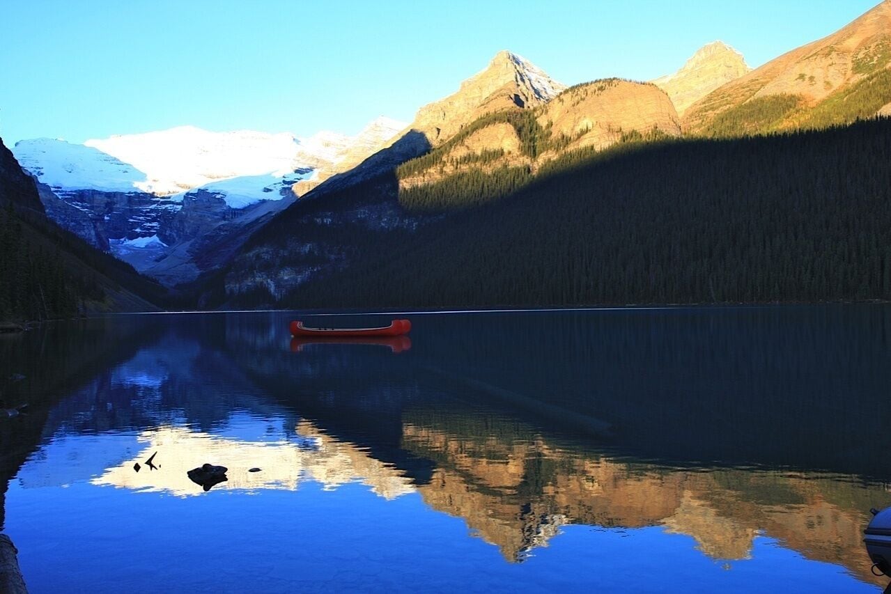 A calm lake with a red canoe in the center, surrounded by mountains and forested areas.