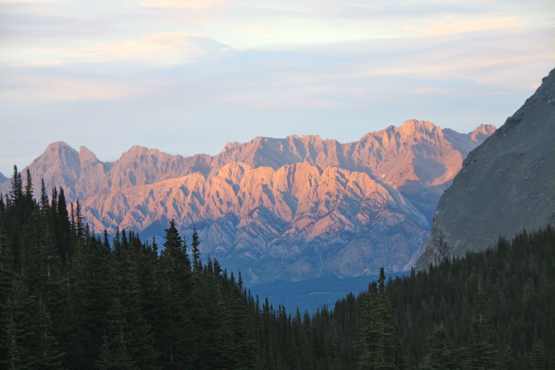A mountainous landscape with dense forests in the foreground and a range of rugged peaks in the background.