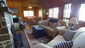 A cozy living room with a stone fireplace, a sofa set, and a dining area. - Linekin Vista - 3BDR Waterfront Cottage on Linekin Bay with Private Beach! (East Boothbay)