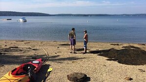 A beach with a kayak, rocky terrain, and a calm lake. - Linekin Vista - 3BDR Waterfront Cottage on Linekin Bay with Private Beach! (East Boothbay)